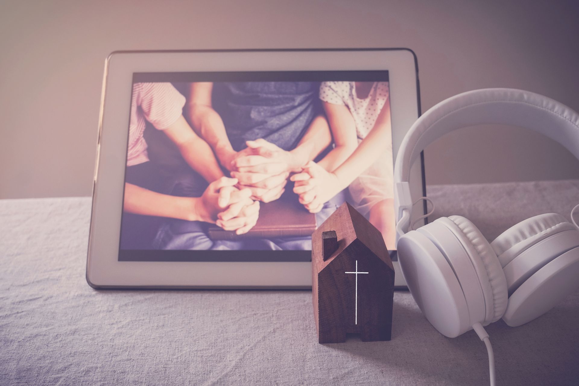 A group of people are praying on a tablet next to a pair of headphones.