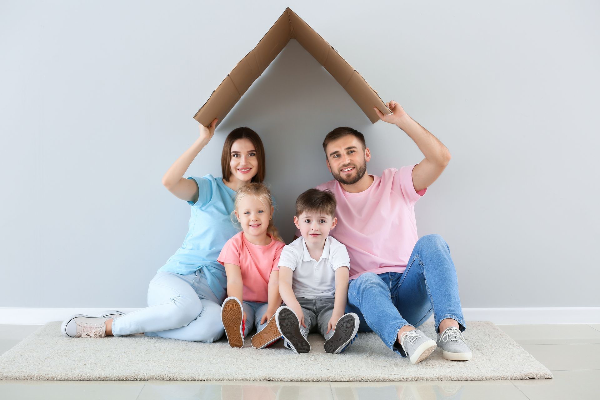 A family is sitting on the floor under a cardboard house.