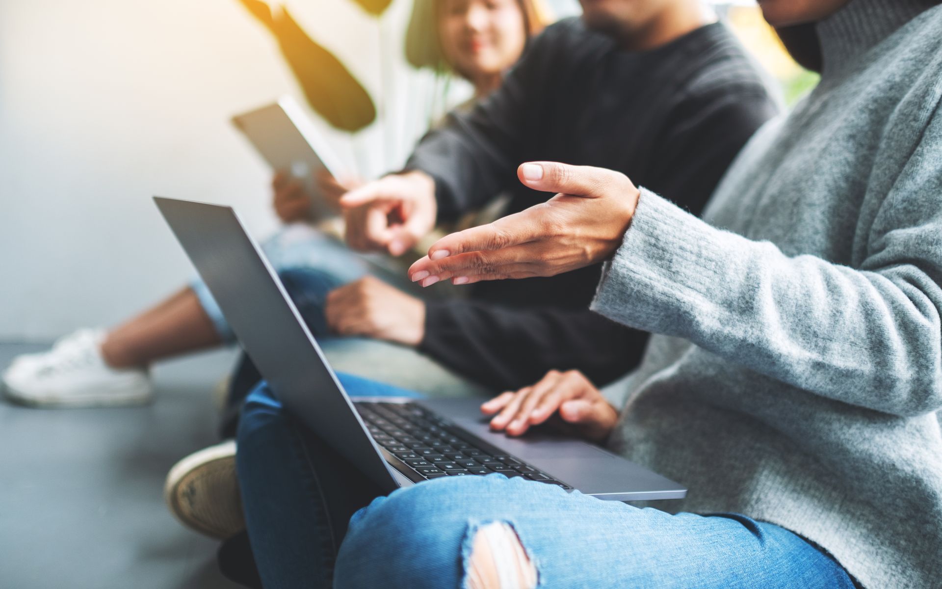 A group of people are sitting on the floor using laptops and tablets.