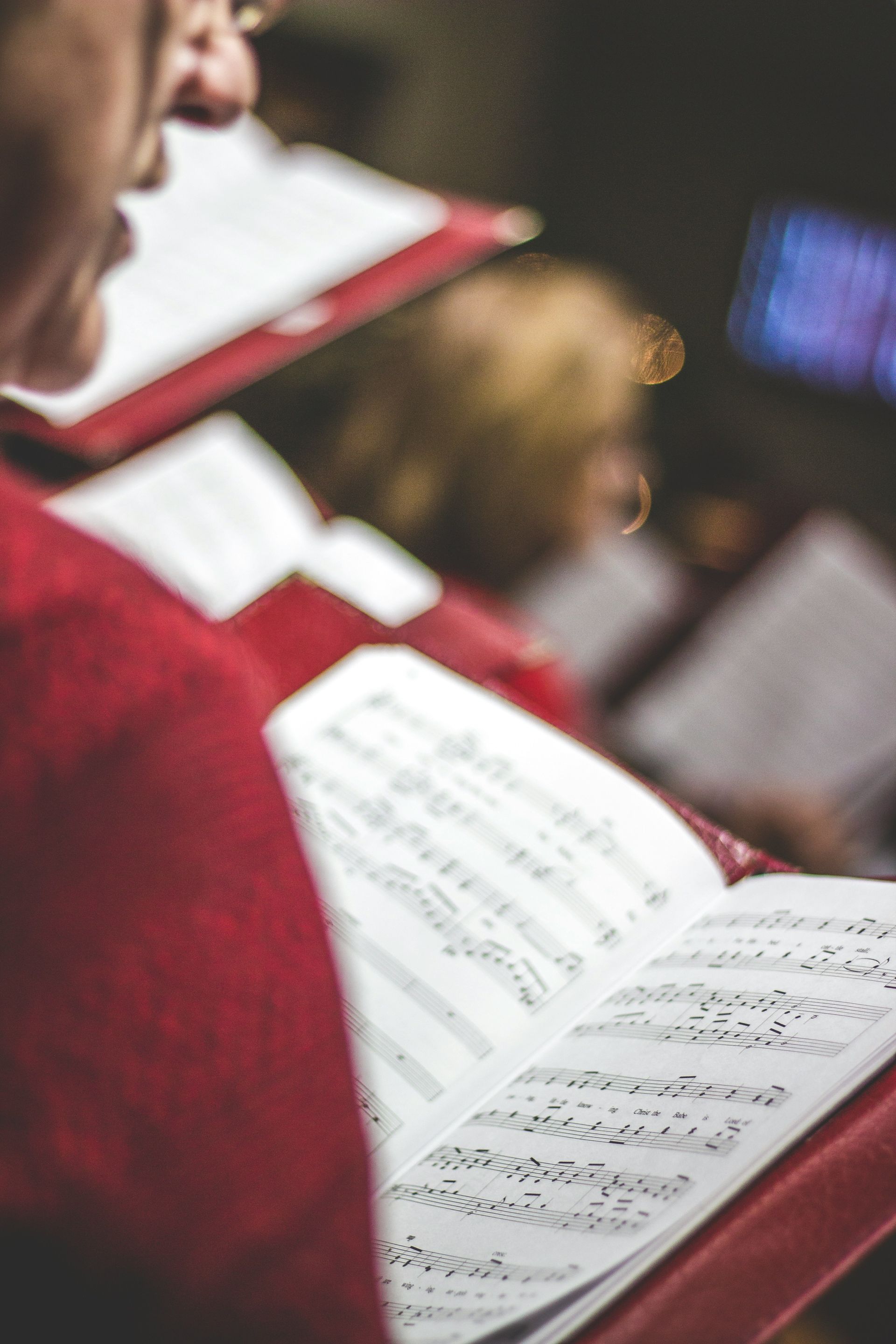 A man in a red sweater is singing in a choir while holding a book of music.