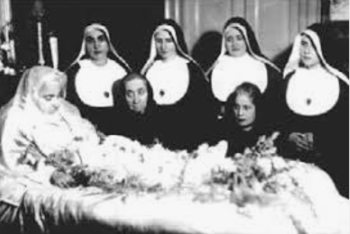 A group of nuns are standing around a coffin.