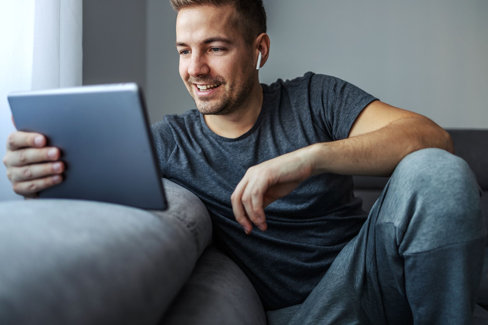 A man is sitting on a couch using a tablet computer.