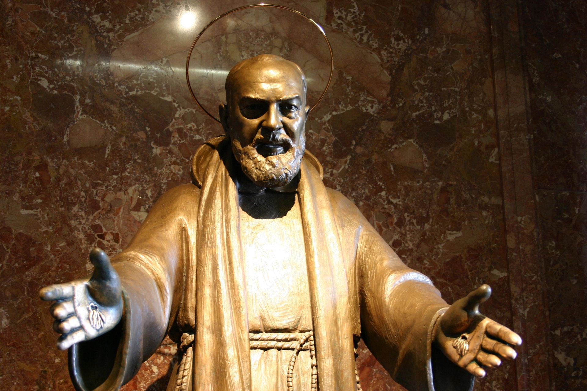 A bronze statue of a Padre Pio with his arms outstretched