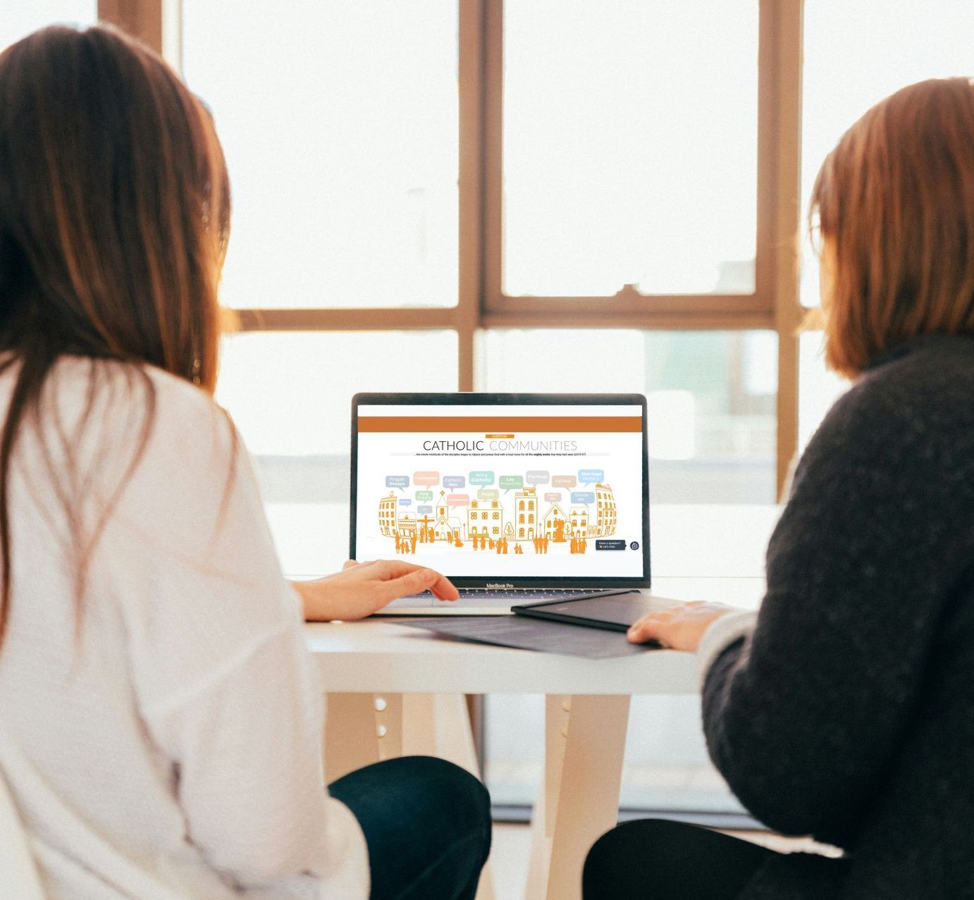 Two women are sitting at a table looking at a laptop