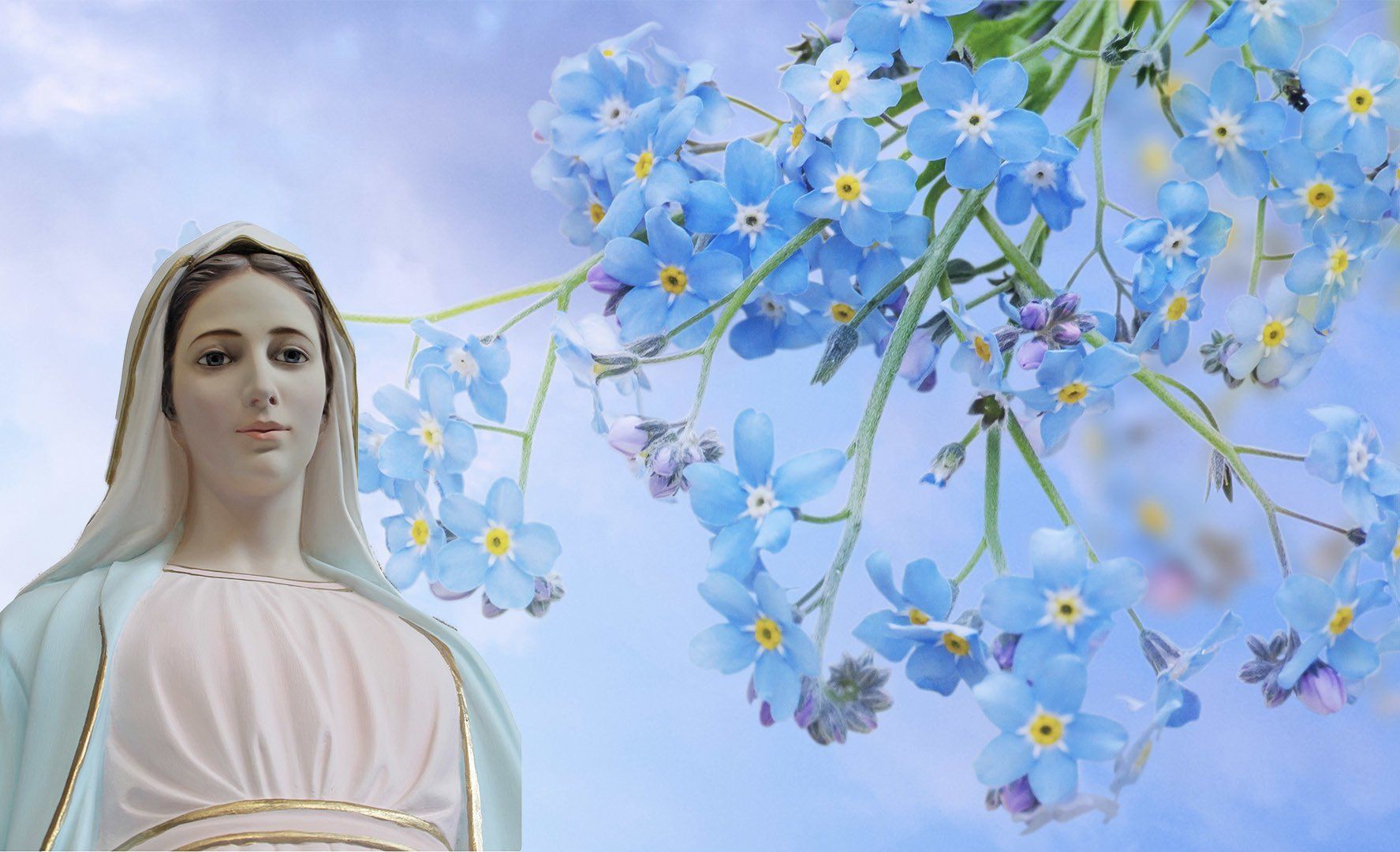 A statue of mary is standing in front of a bunch of blue flowers.