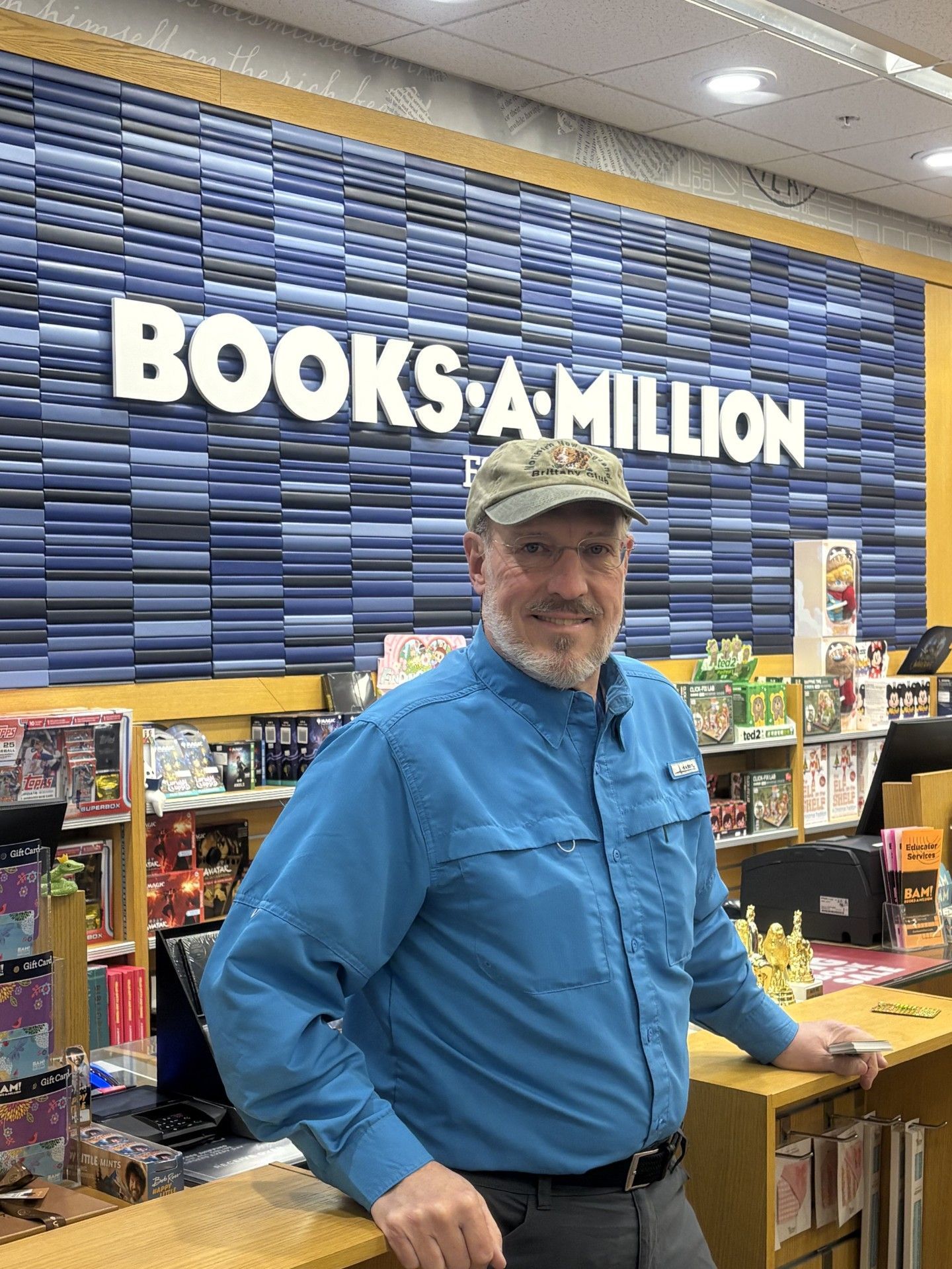Man in blue shirt, hat, at Books-A-Million counter, smiling.