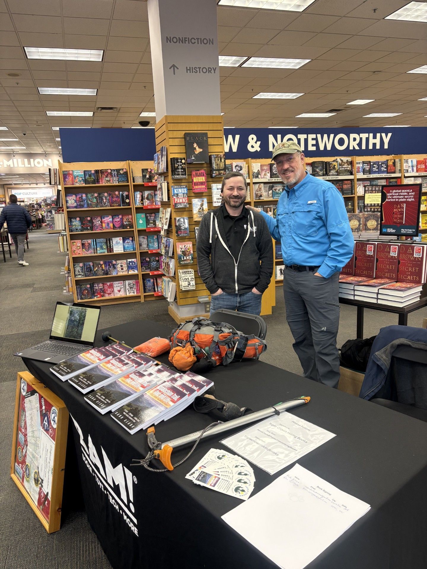 Two men at a book signing table. Bookstore setting, books in the background.