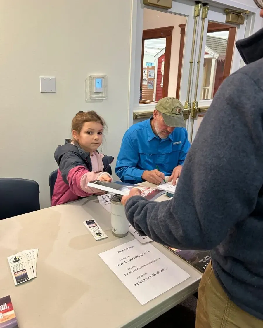 A young girl, an older man and another person at a table, likely signing up for an event or receiving information.