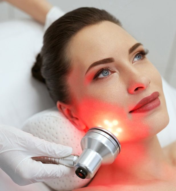 Woman is Getting a Red Light Treatment on Her Face — Gladstone Beauty Clinic In Gladstone Central, QLD