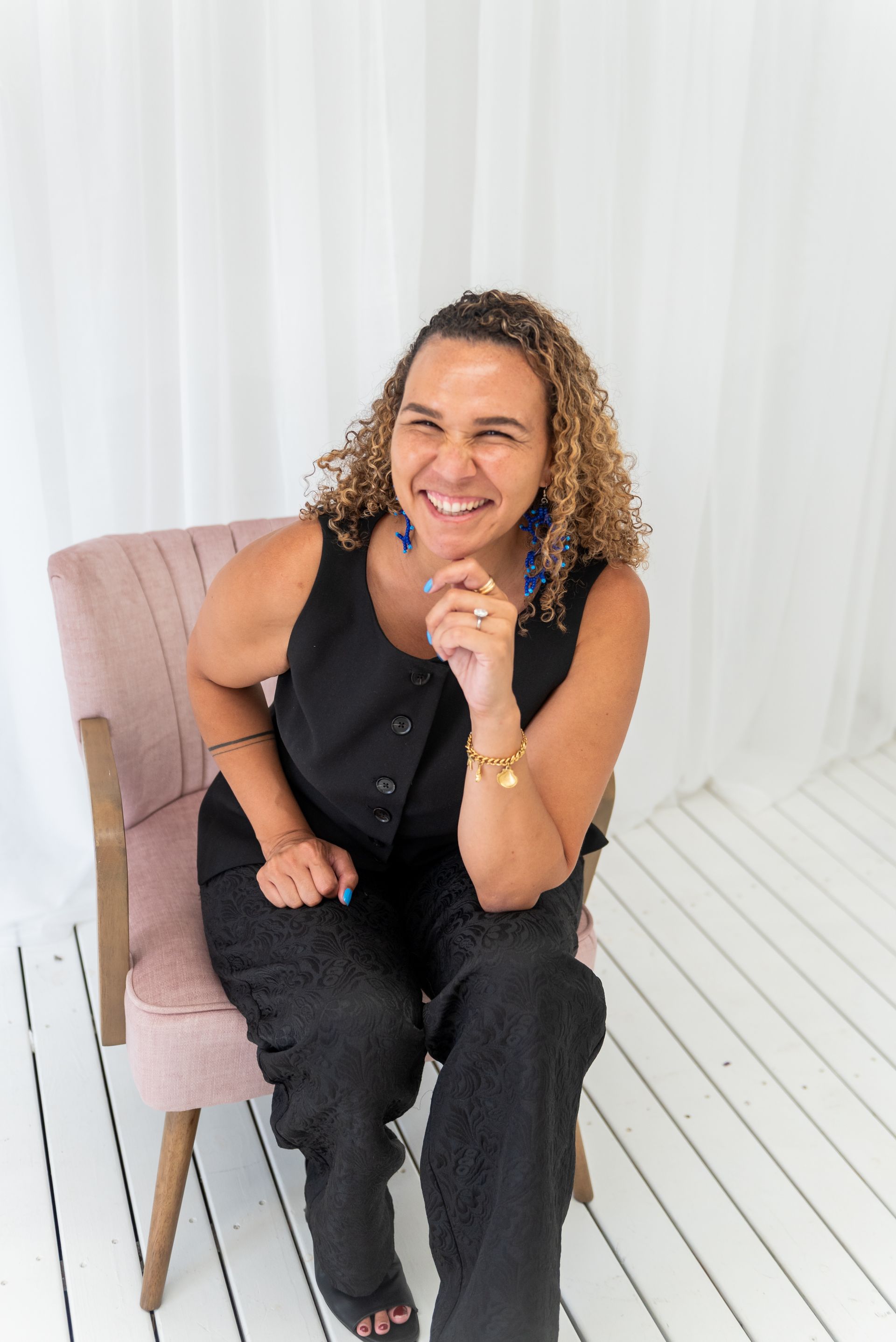 Libby Cook-Black sits smiling in pink chair. White background