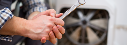 Un hombre sostiene una llave inglesa delante de un ventilador.