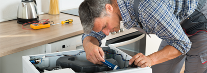 Un hombre está trabajando en una lavadora en una cocina.