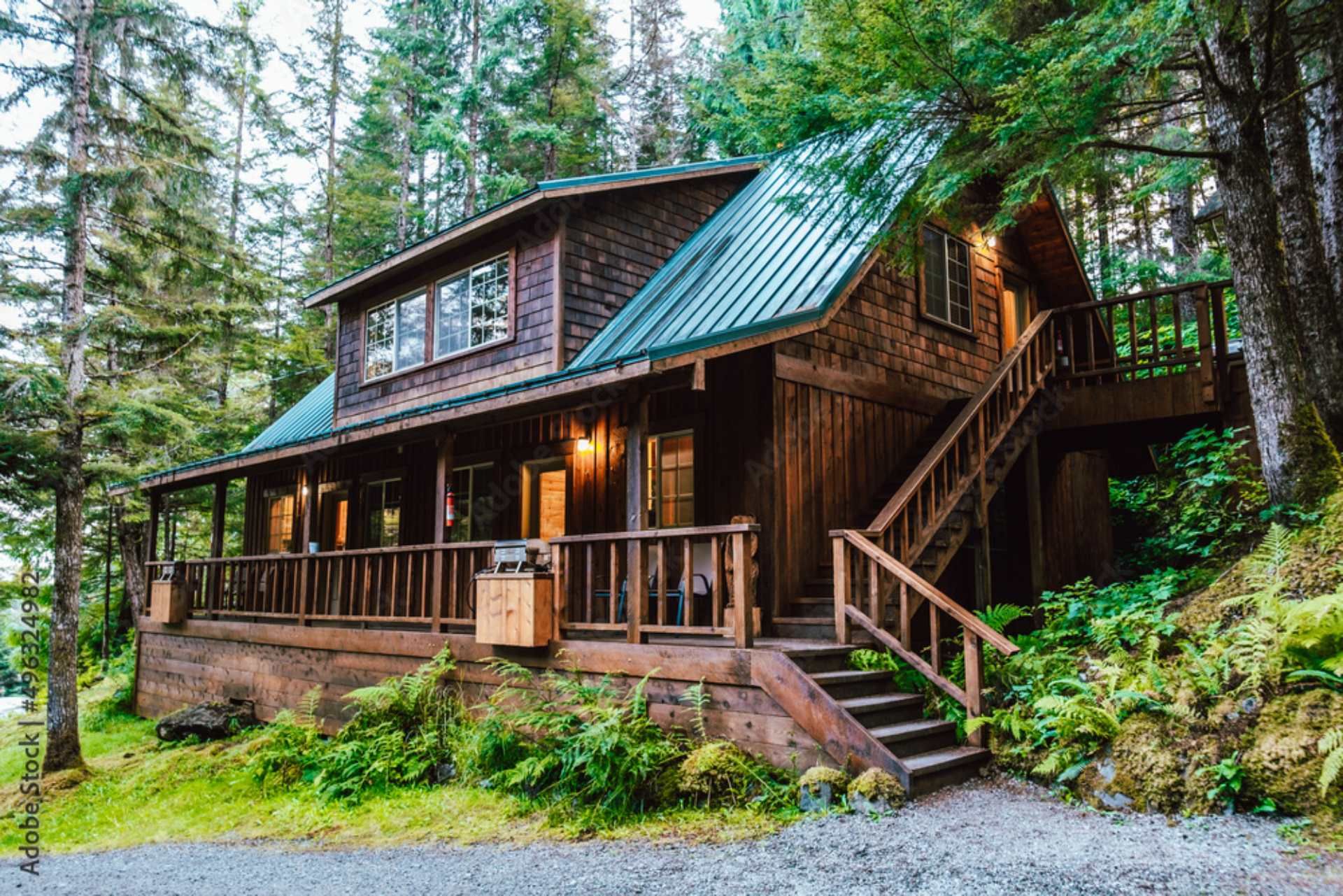 A large wooden house with a green roof is surrounded by trees.