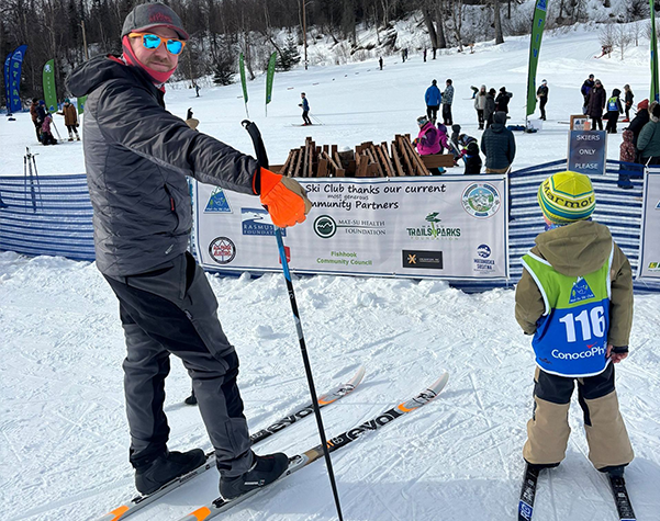 A man is teaching a child how to ski in the snow.