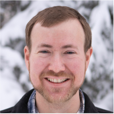 A man with a beard is smiling in front of snowy trees