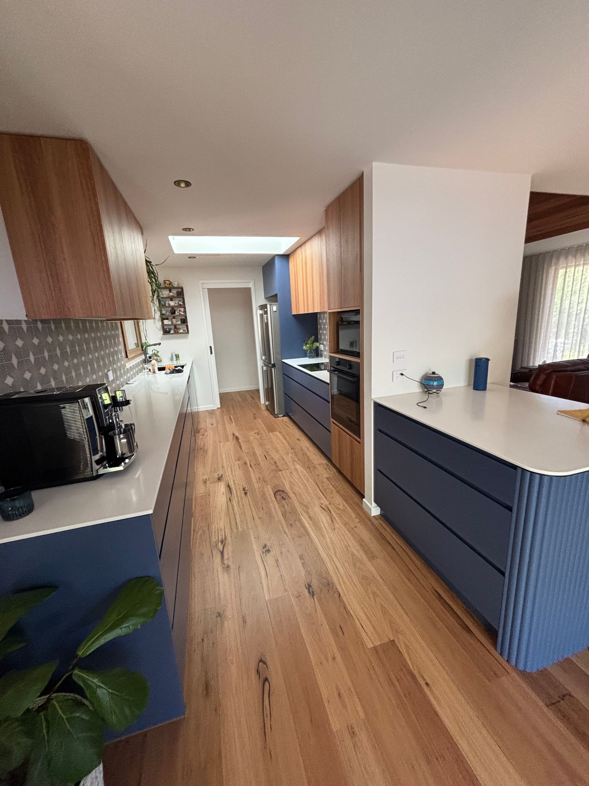 Modern kitchen with blue and wood cabinets, white countertops, and wood flooring.