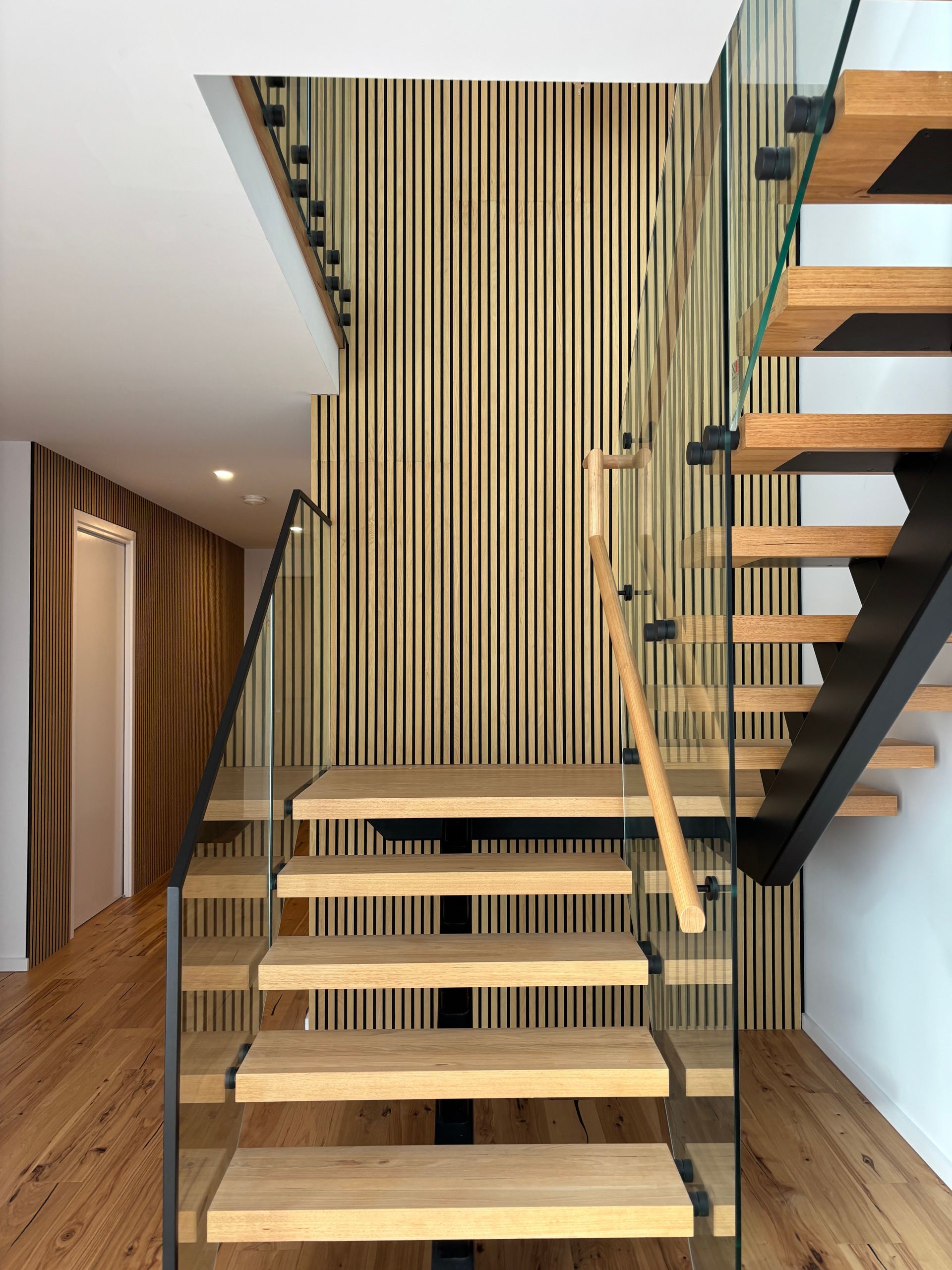 Wooden staircase with glass railings and wood-paneled wall.