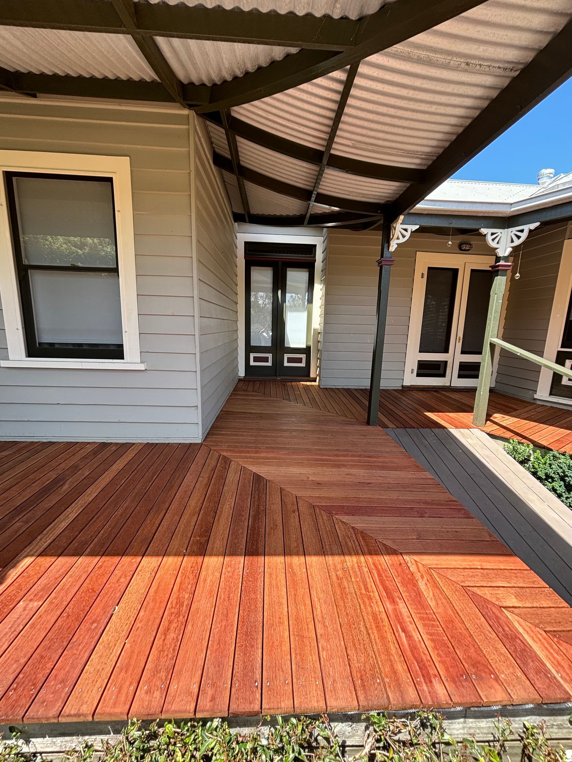 Wooden deck and porch of a gray house, featuring a corrugated metal roof.
