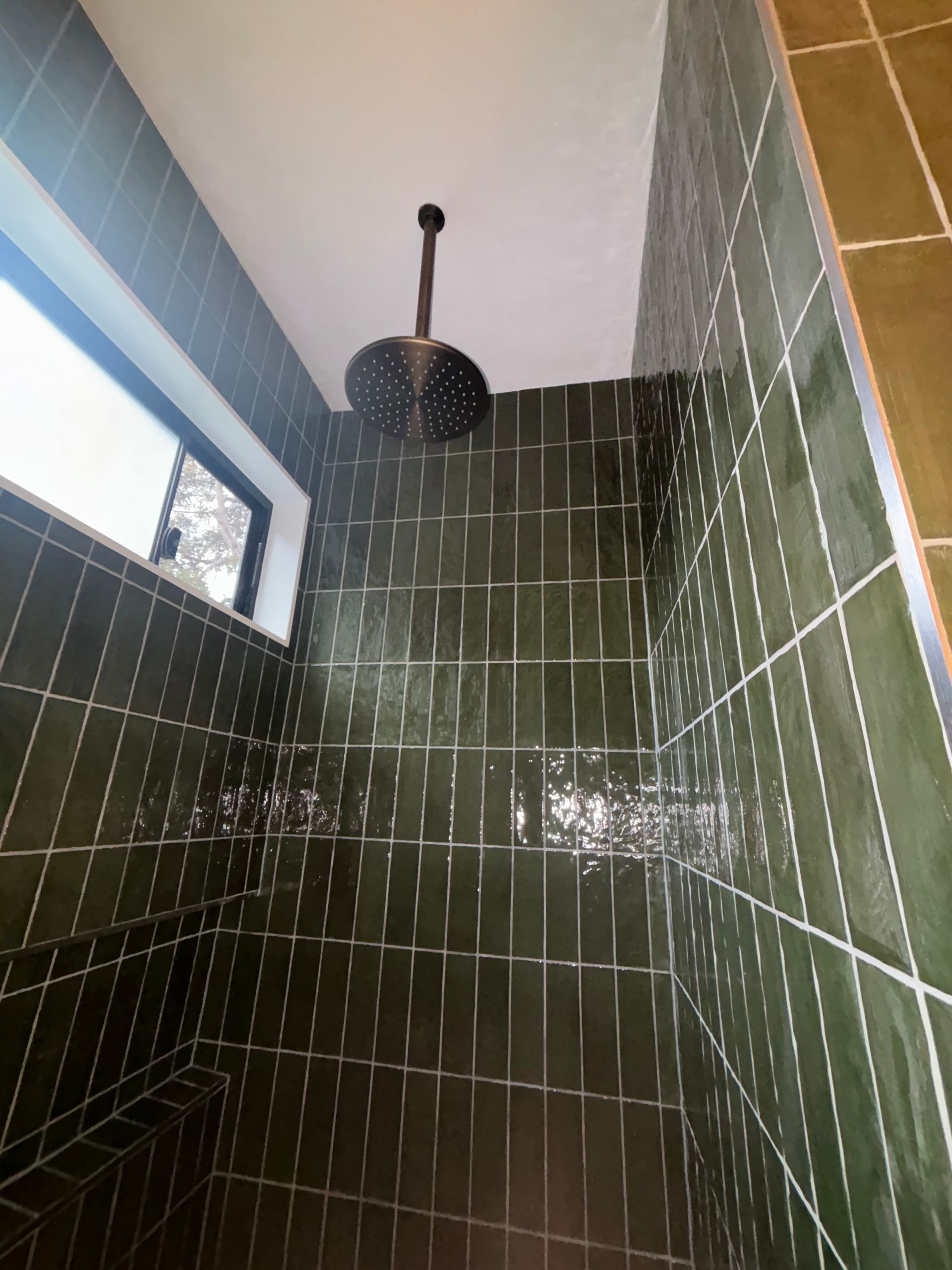 A shower with green tiles and a black shower head