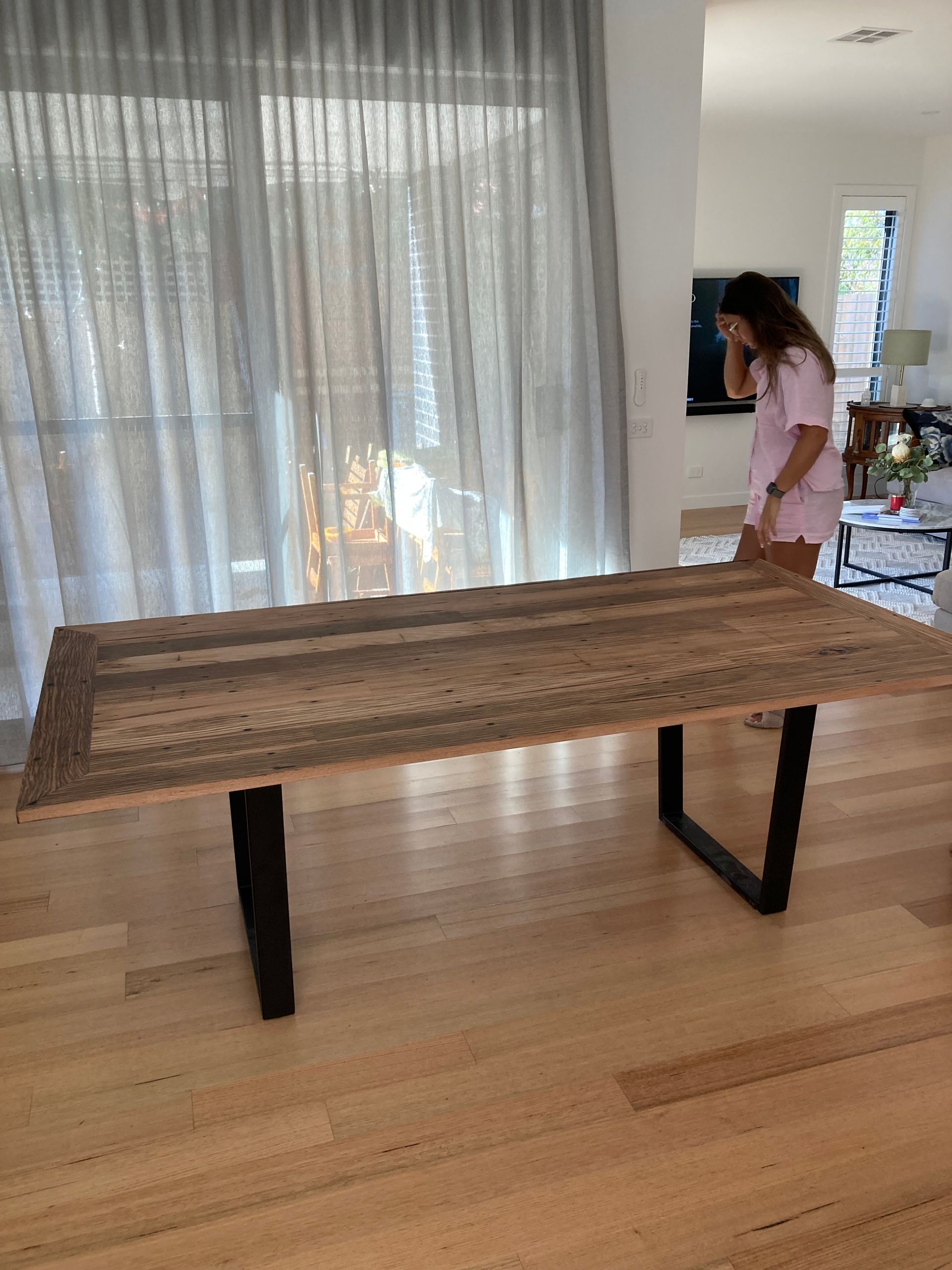 A woman is standing next to a wooden table in a living room.