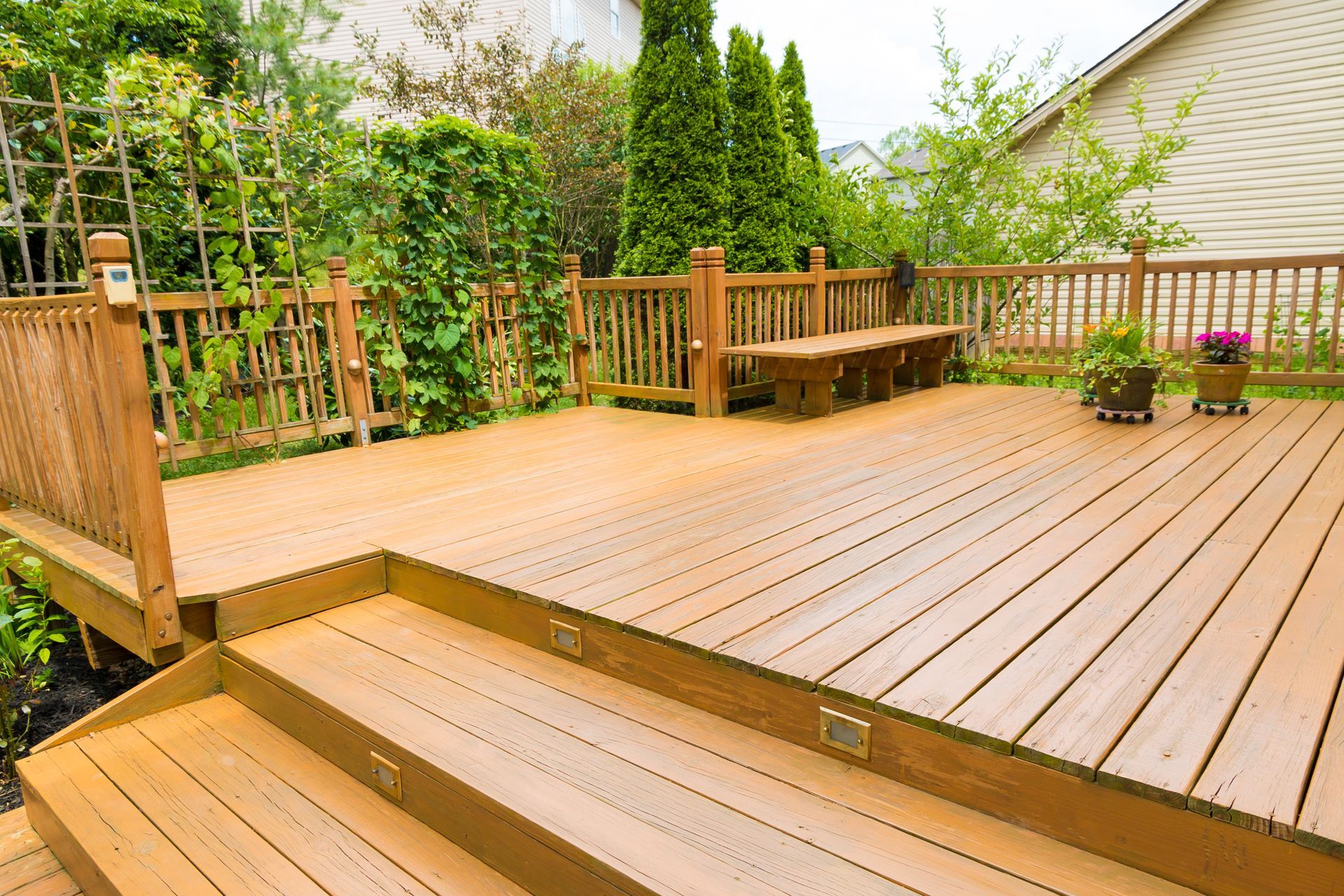 Wooden deck with steps, potted plants, bench, and surrounding greenery.