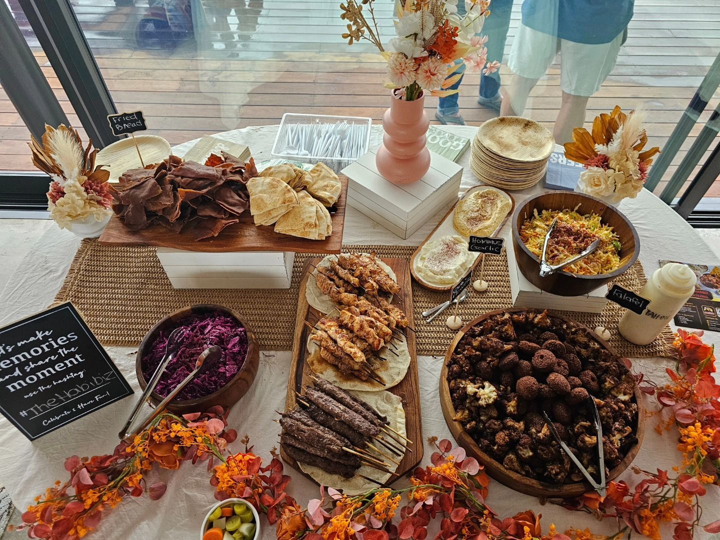 A food spread with various dishes: chips, tacos, salads, and flowers. Brown and orange colours dominate. - The Habibiz Catering in Wingham NSW