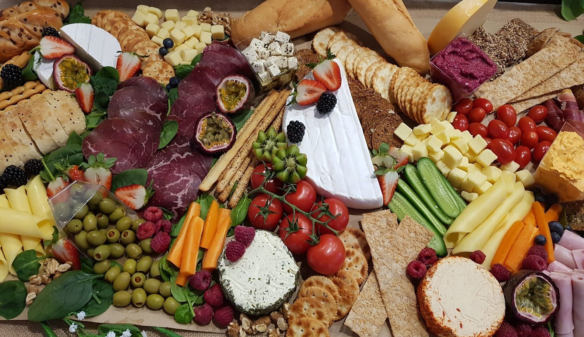 Charcuterie board with cheese, meats, fruits, vegetables, and crackers arranged for a gathering. - The Habibiz Catering in Wingham NSW