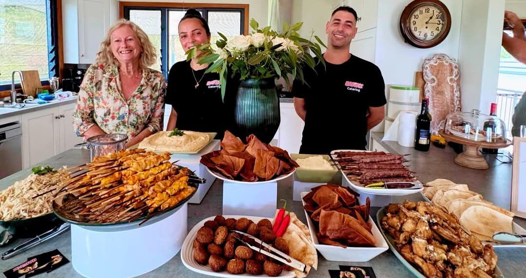 People standing behind a table of catered food. Indoor setting. — The Habibiz Catering In Wingham, NSW