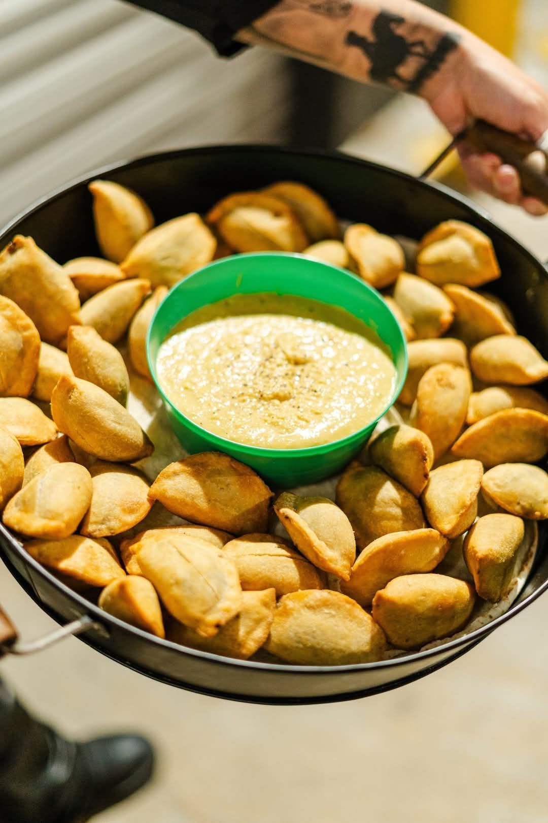 Person holding a pan filled with golden-brown empanadas, green bowl of sauce in the center. — The Habibiz Catering In Wingham, NSW