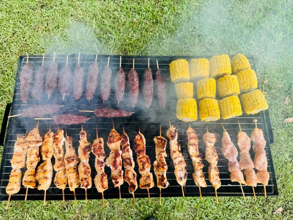 Grilled meat skewers and corn on the cob on a black grill outdoors, on green grass. - The Habibiz Catering in Wingham NSW