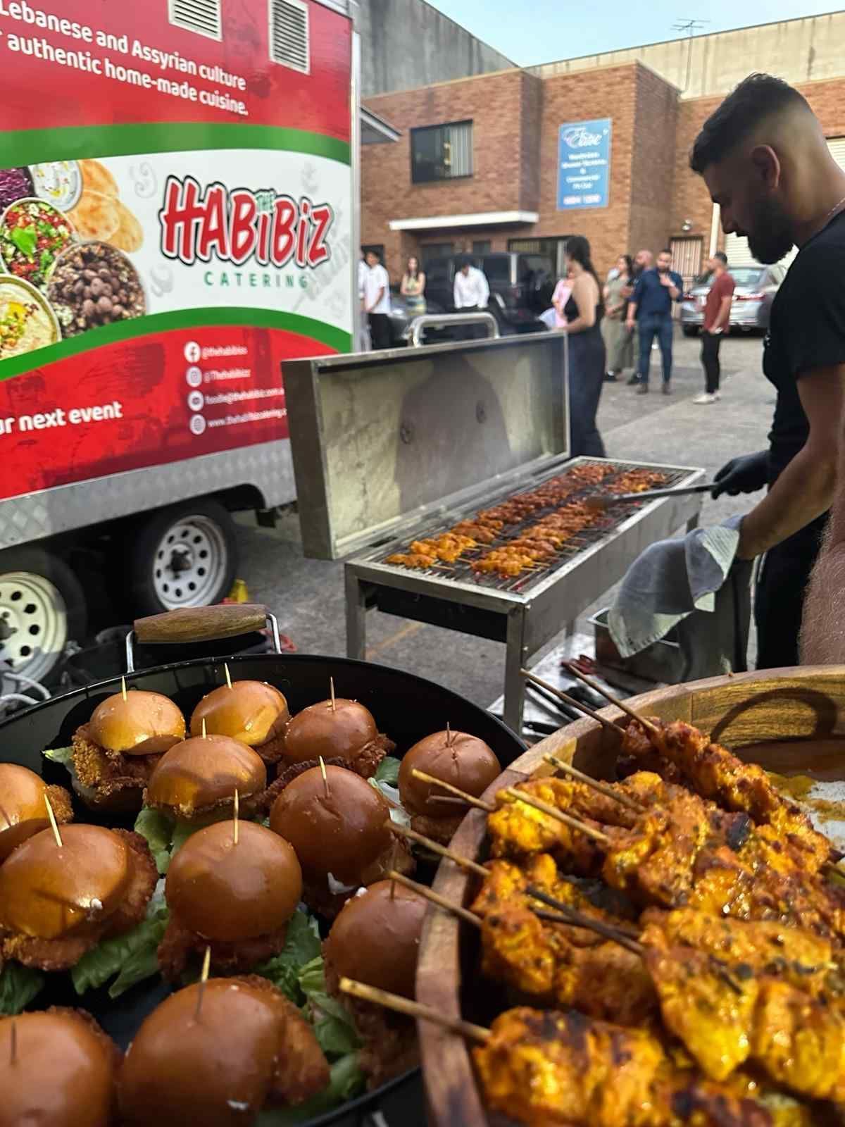 Food truck catering event: grill with skewers, burgers. Man grilling outdoors; people waiting. - The Habibiz Catering in Wingham NSW