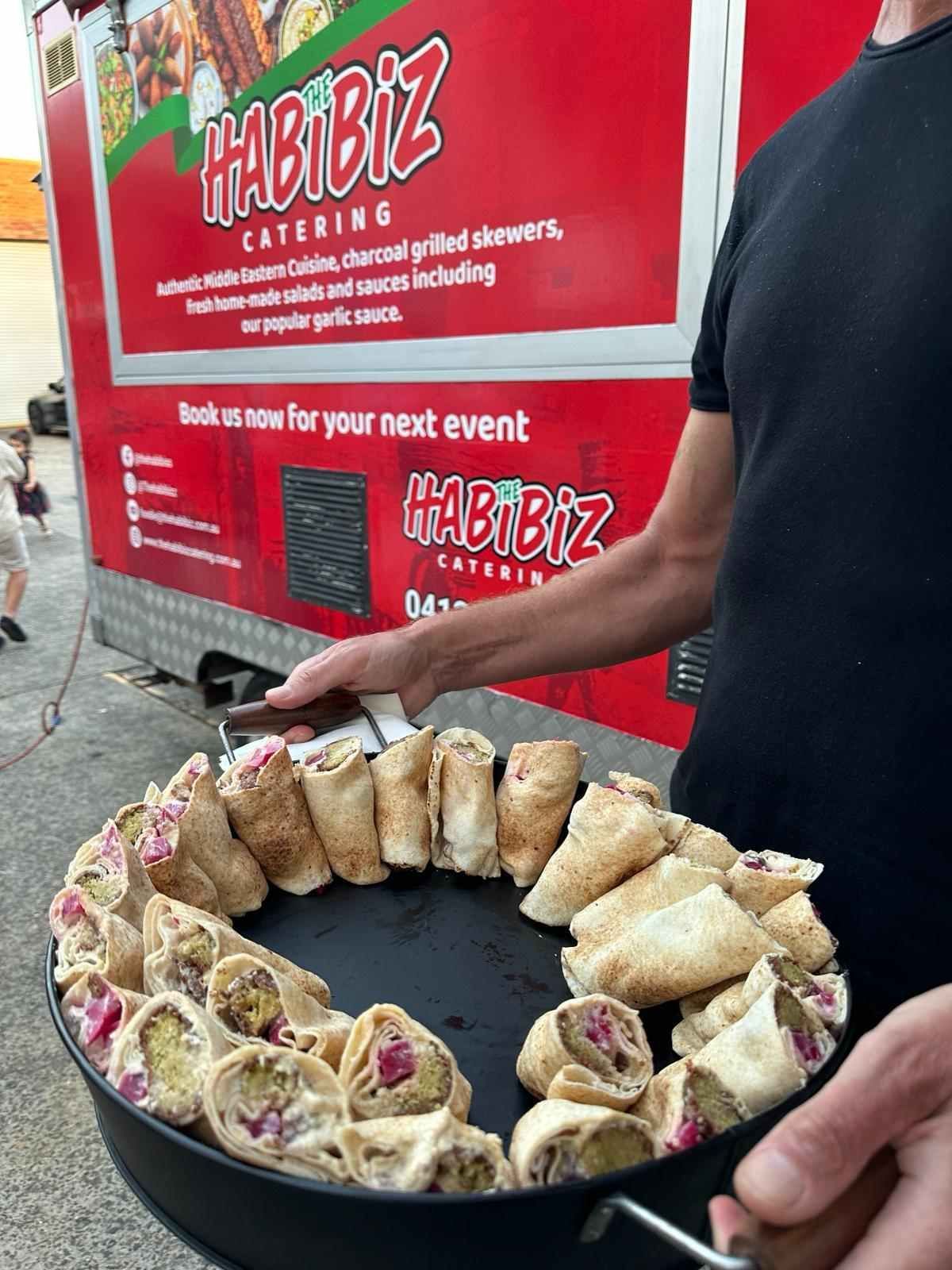 A Person Holding a Platter of Middle Eastern Wraps in Front of A Food Truck — The Habibiz Catering in Taree, NSW