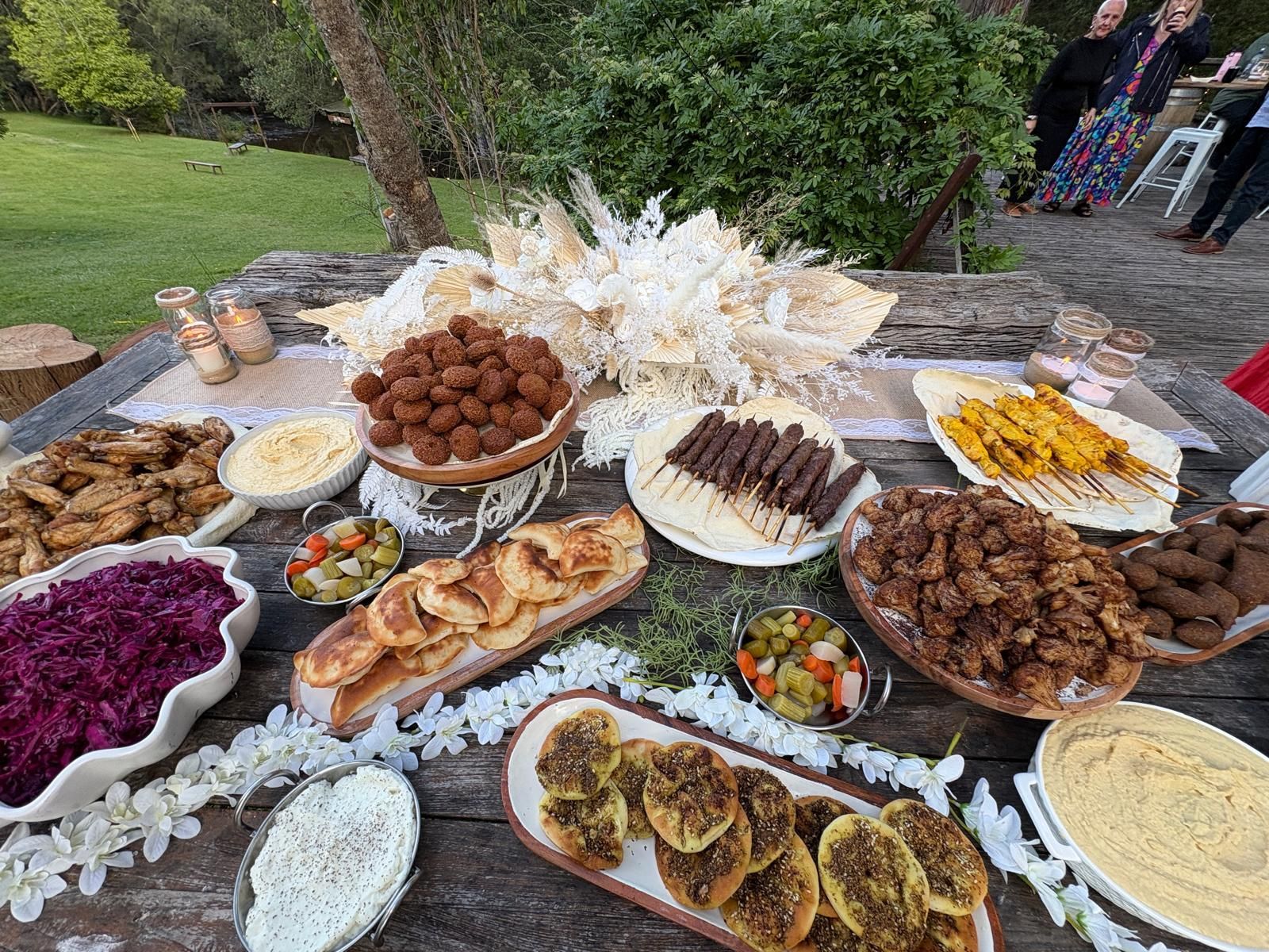 Outdoor table laden with Middle Eastern food, including falafel, skewers, dips, and salads. — The Habibiz Catering In Wingham, NSW