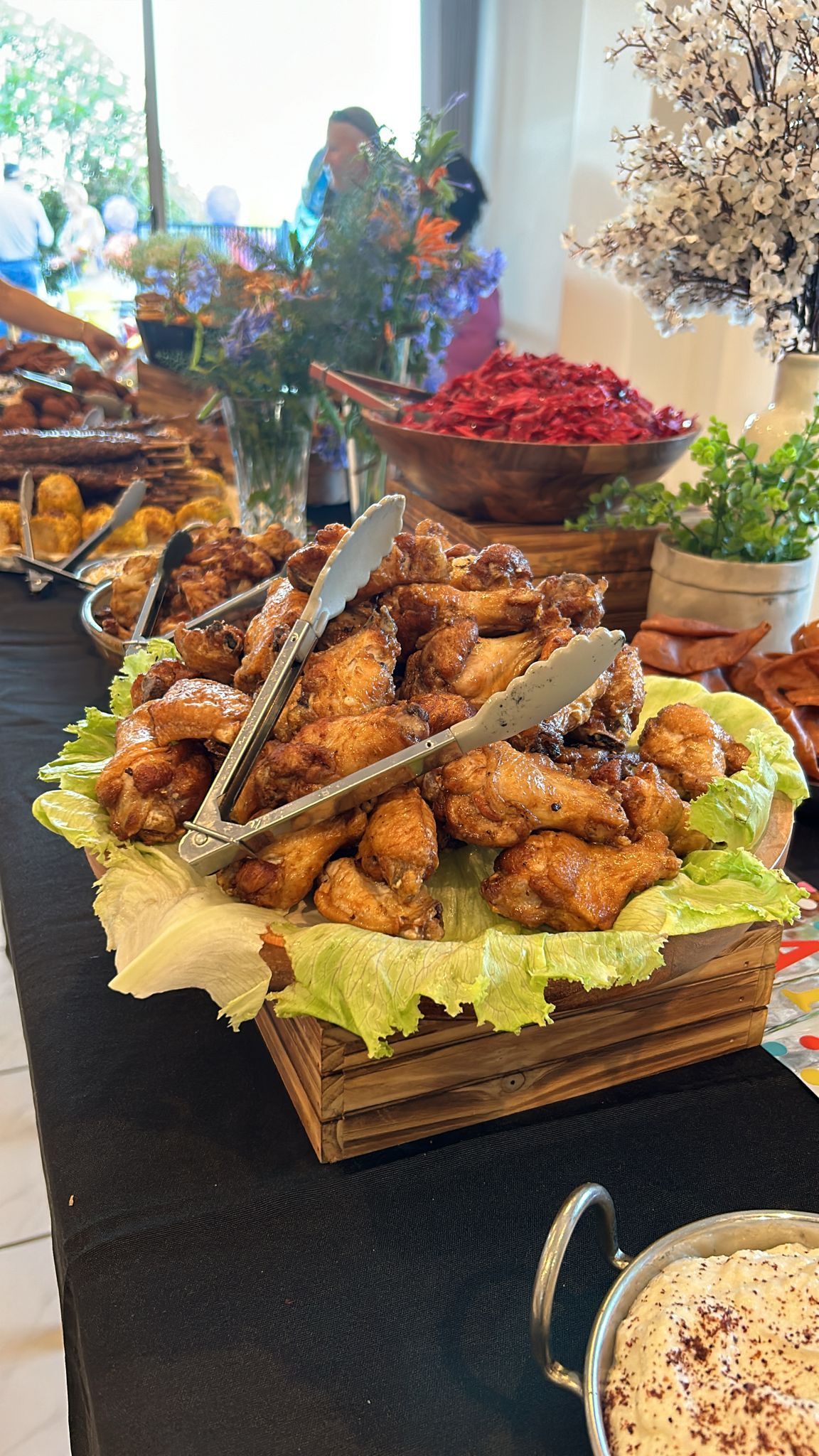 Buffet table with fried chicken wings on lettuce in a basket; other food items in the background. — The Habibiz Catering In Wingham, NSW