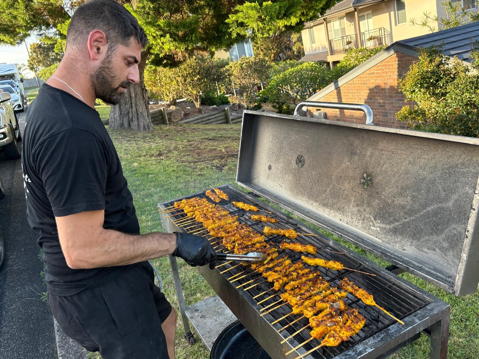 Man grilling skewers outdoors, using tongs, on a charcoal grill. — The Habibiz Catering In Wingham, NSW