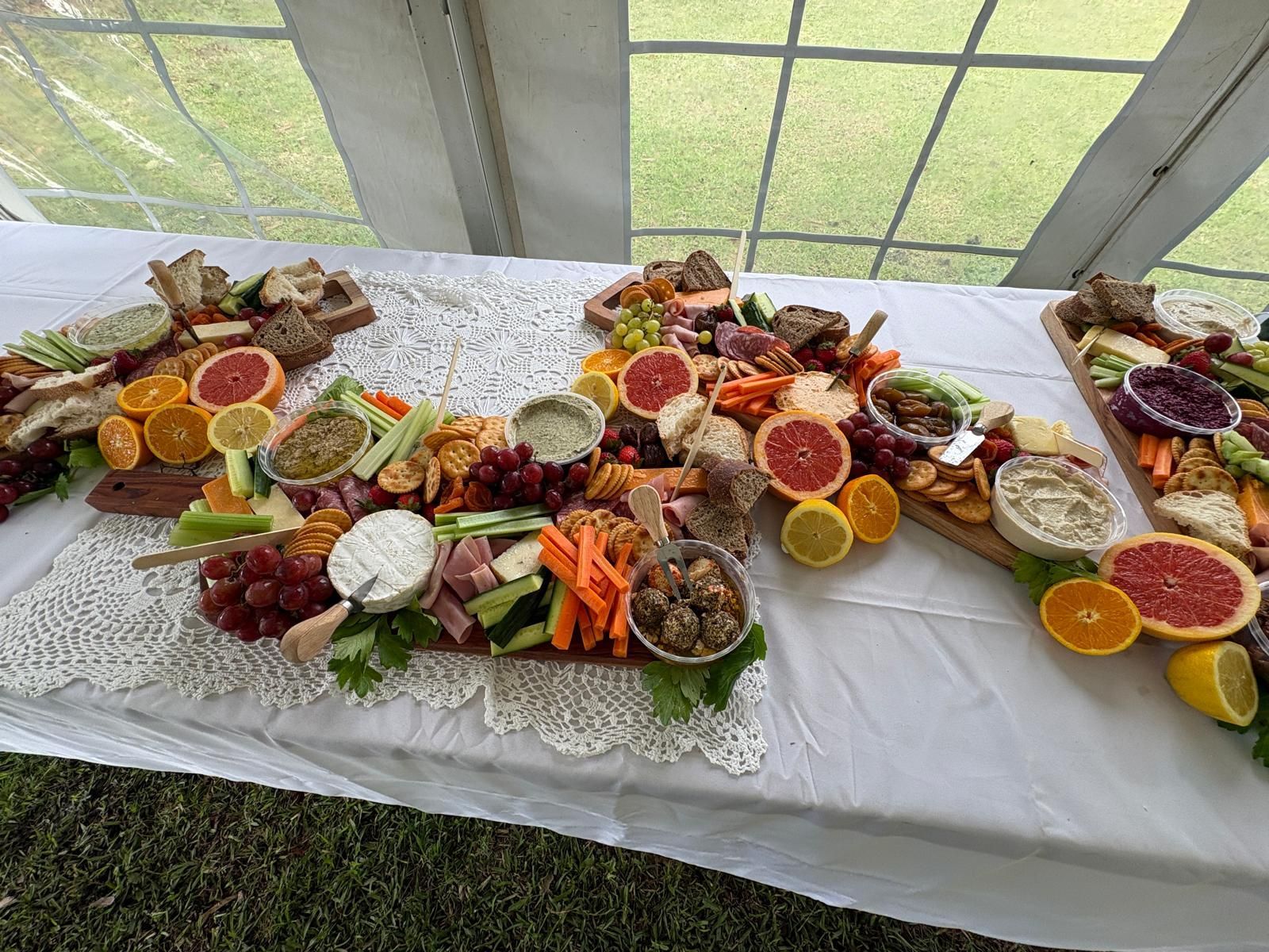 Charcuterie boards with various cheeses, fruits, and vegetables on a white table under a tent. — The Habibiz Catering In Wingham, NSW