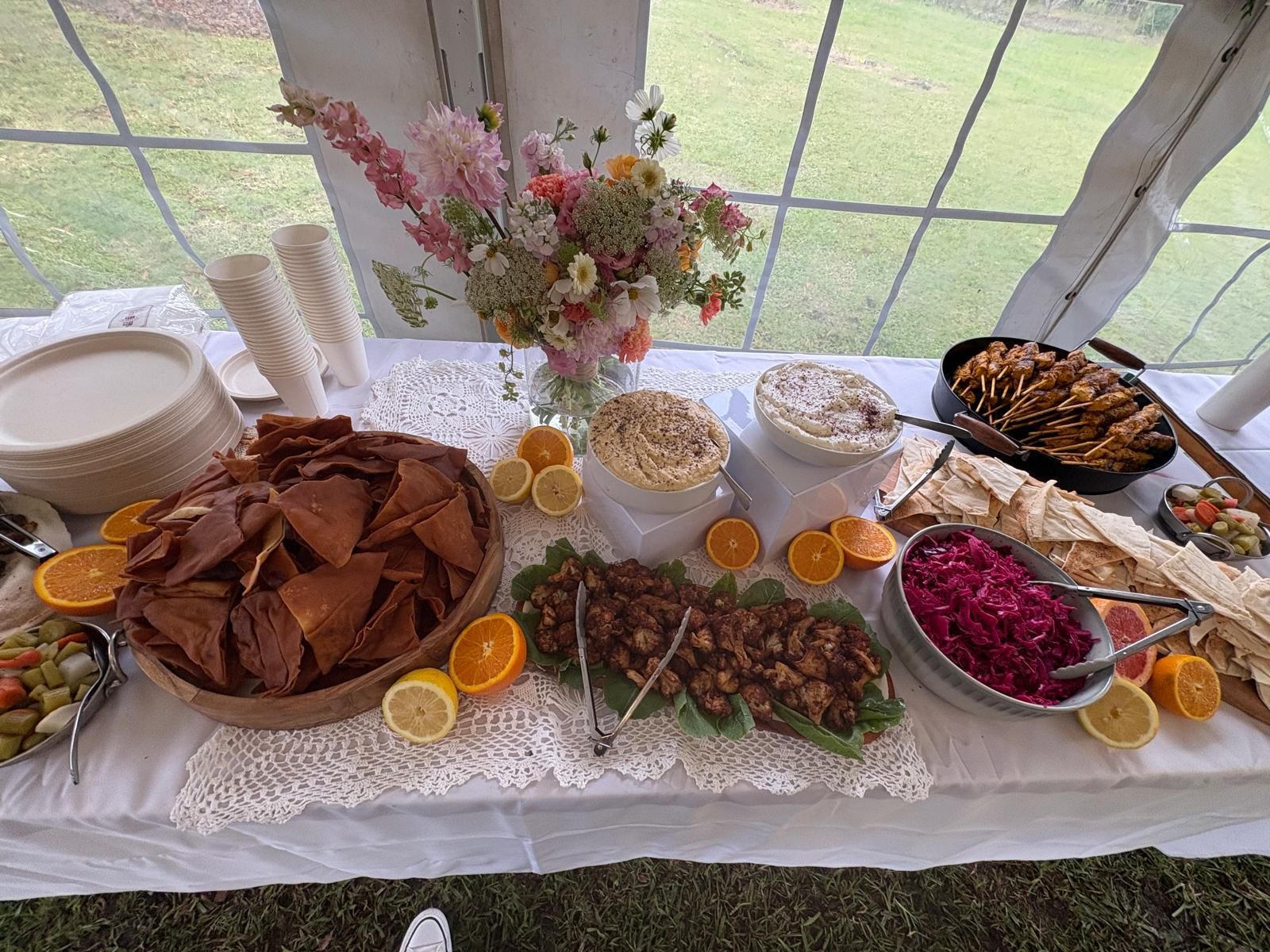 Buffet table with various dips, chips, and garnishes, including flowers and citrus fruit. — The Habibiz Catering In Wingham, NSW