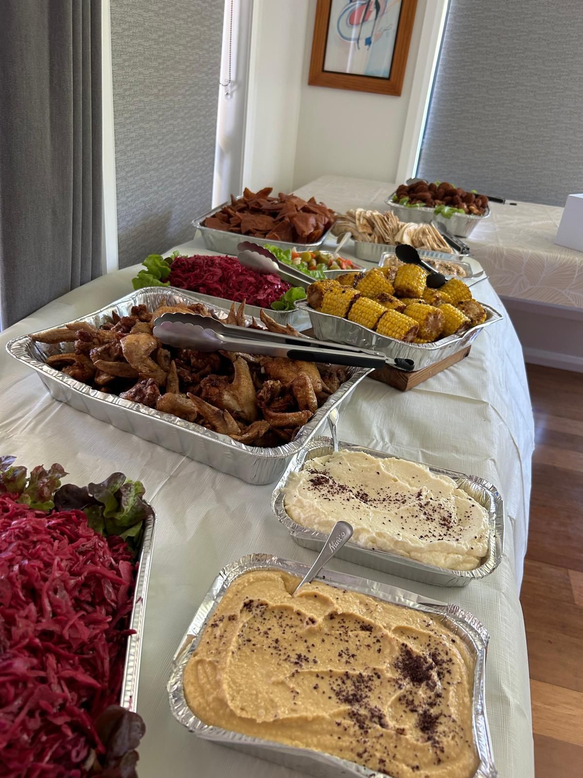 Buffet table with various dishes including hummus, fried food, and corn on the cob. — The Habibiz Catering In Wingham, NSW
