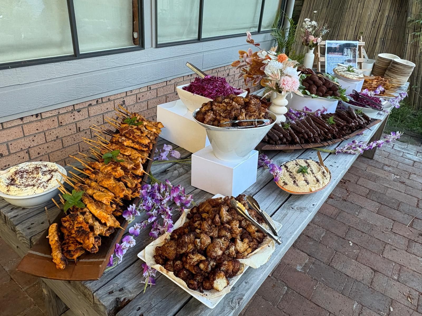 Buffet table with various foods: kebabs, dips, and salads, decorated with flowers. — The Habibiz Catering In Wingham, NSW
