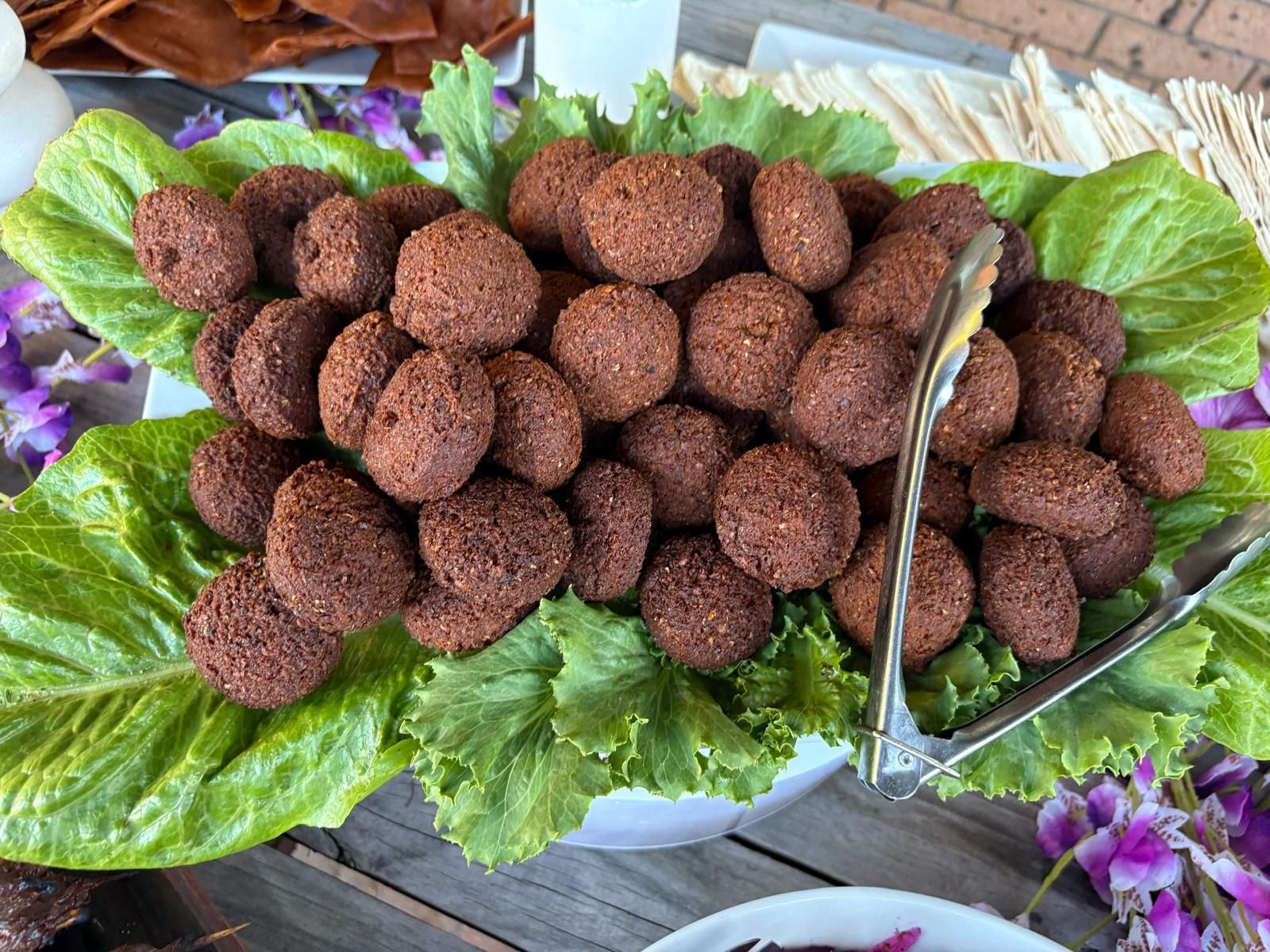 Falafel balls on a bed of lettuce, served with tongs. — The Habibiz Catering In Wingham, NSW