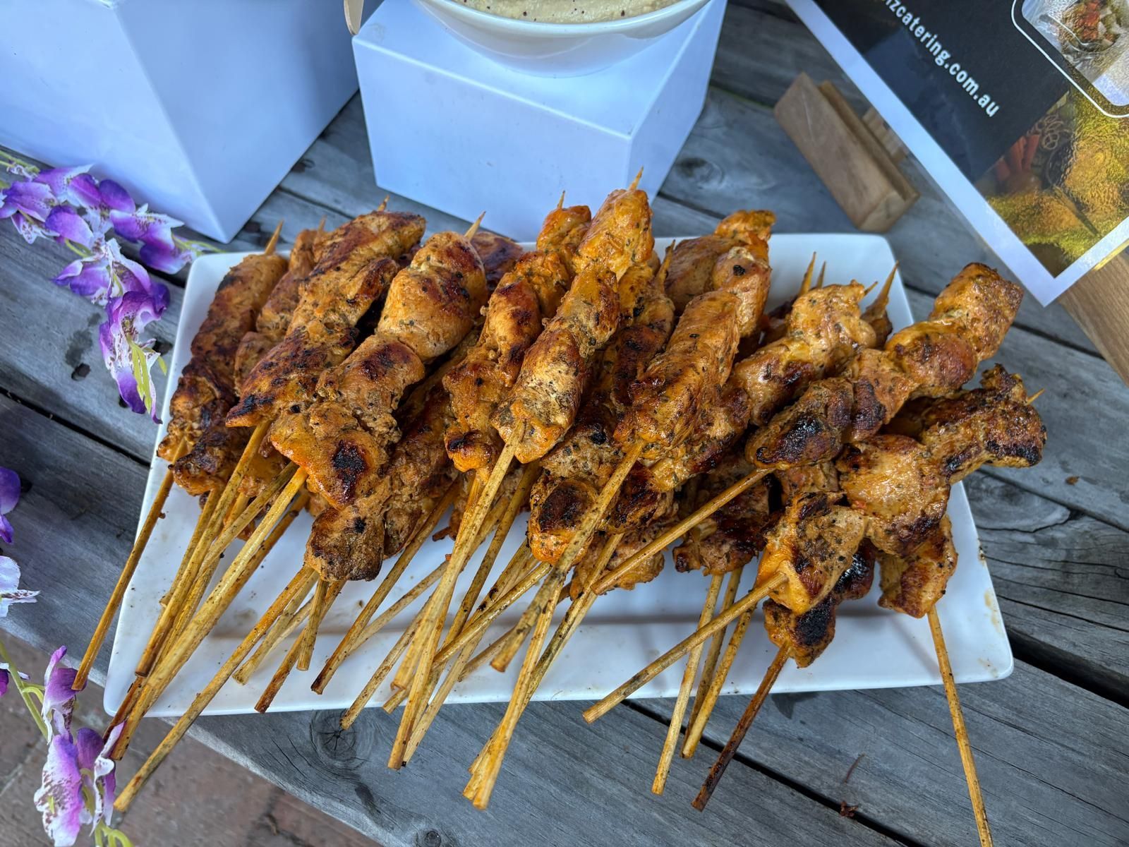 Grilled chicken skewers on a white rectangular plate, outdoor setting. — The Habibiz Catering In Wingham, NSW