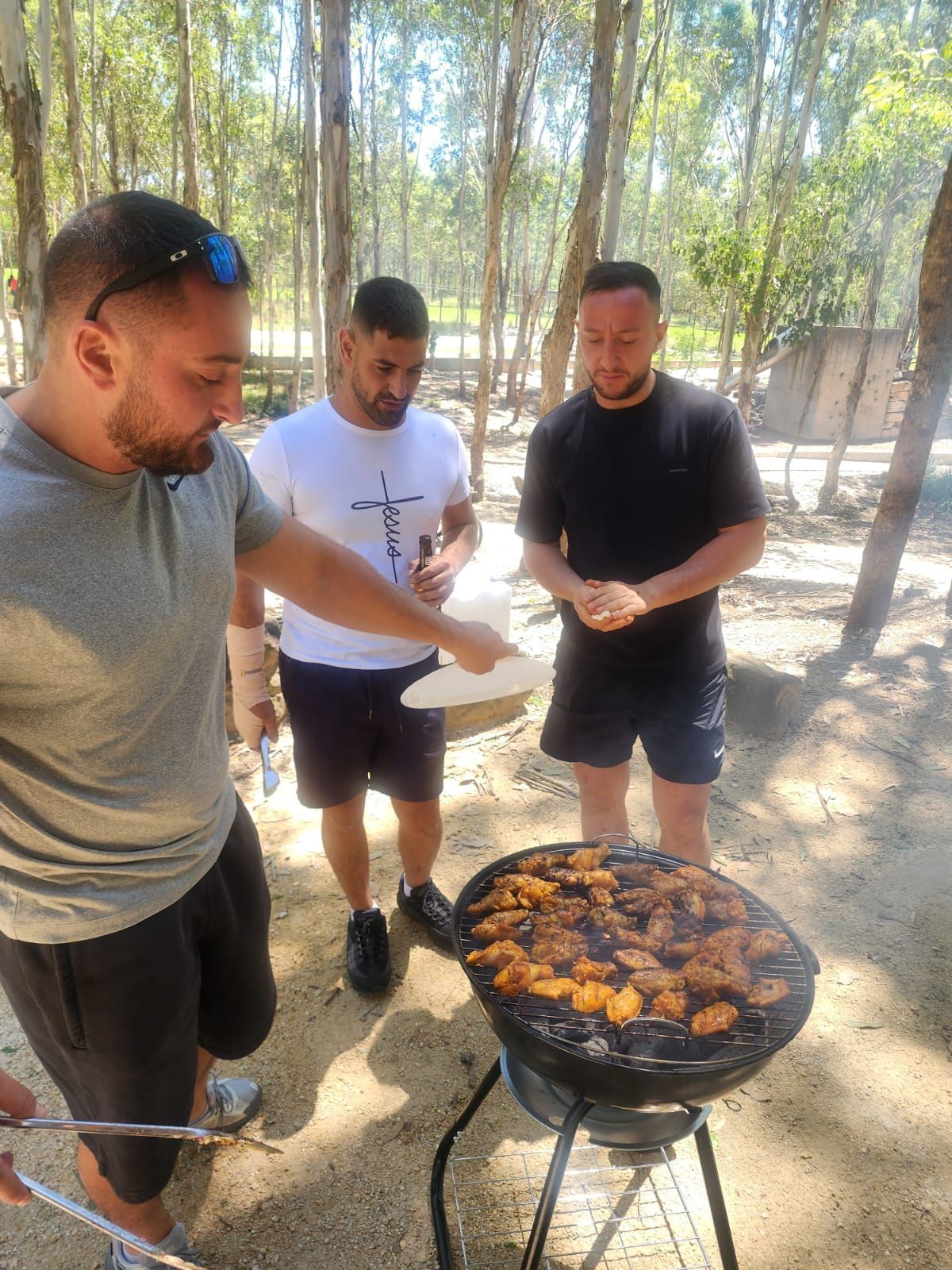 Three people grilling food on a charcoal grill outdoors. One points, others observe. — The Habibiz Catering In Wingham, NSW
