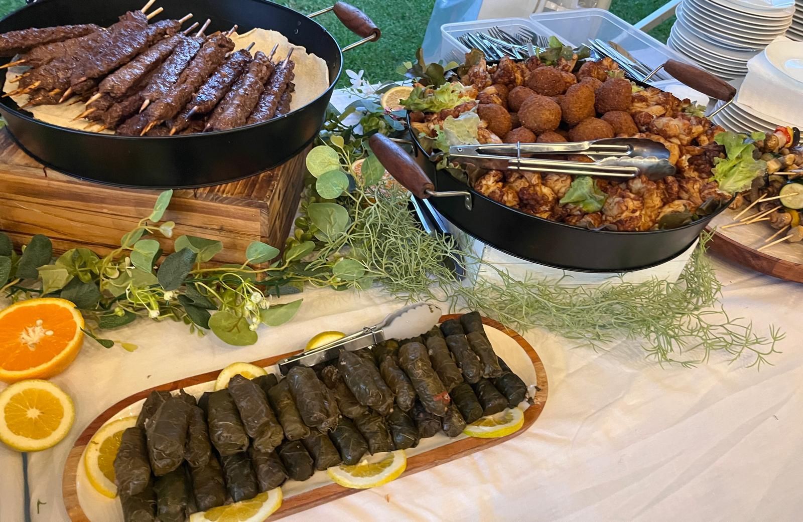 A buffet table with Middle Eastern food, including skewers, falafel, and stuffed grape leaves, decorated with greenery and citrus. — The Habibiz Catering In Wingham, NSW