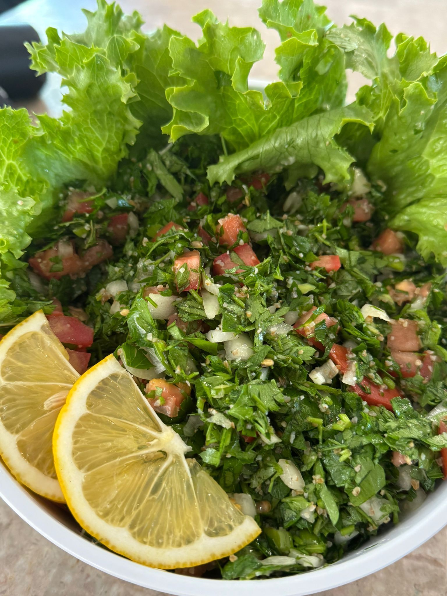 Tabbouleh salad with tomatoes, parsley, and lemon wedges in a white bowl. — The Habibiz Catering In Wingham, NSW
