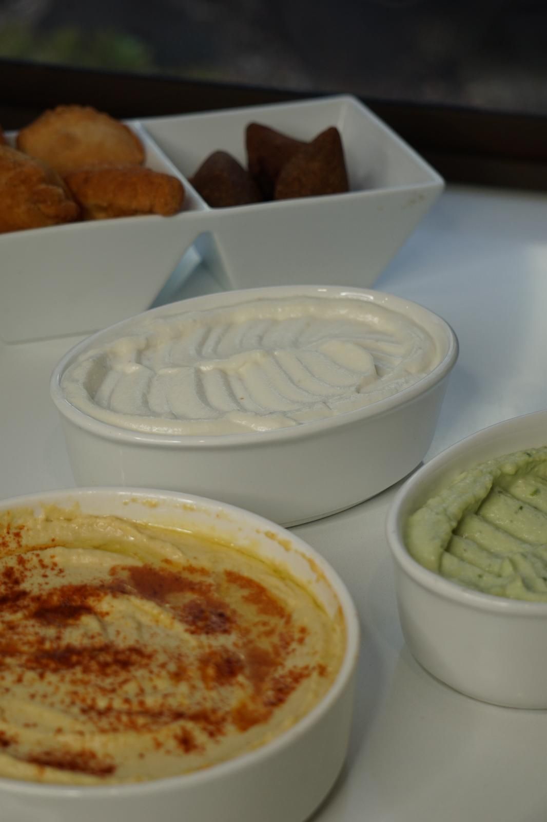 Bowls of hummus, yogurt dip, and green dip; falafel and pastries in the background. - The Habibiz Catering in Wingham NSW