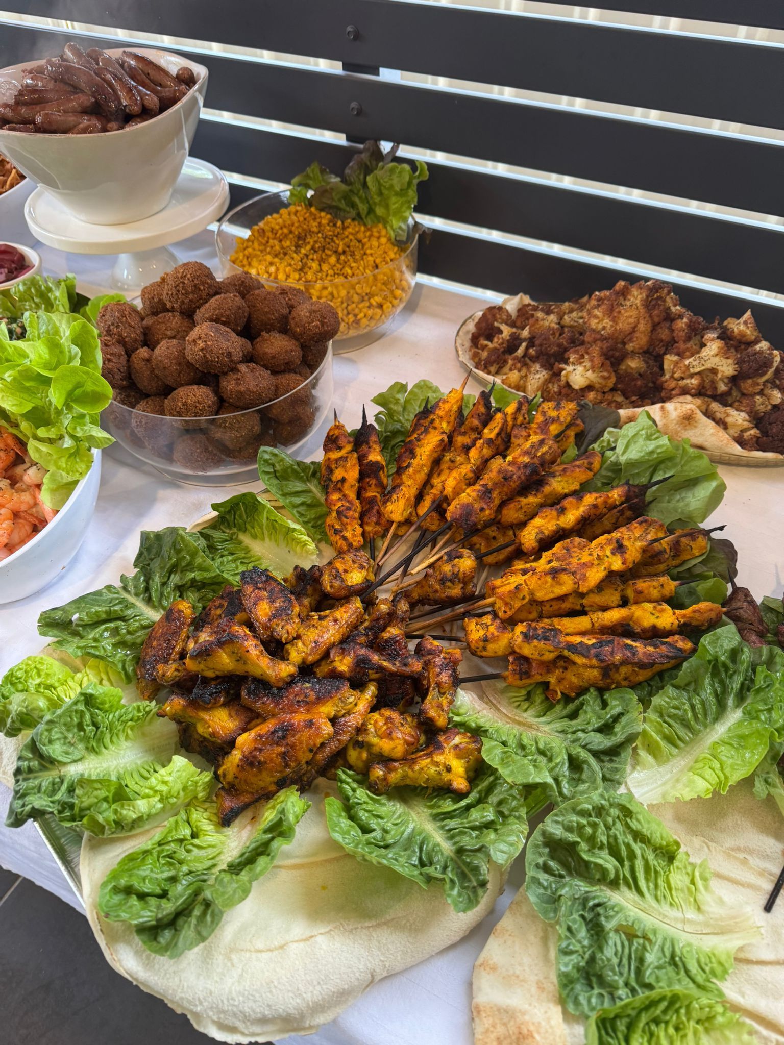 Spread of Middle Eastern food: grilled chicken skewers and other dishes on a white table. - The Habibiz Catering in Wingham NSW