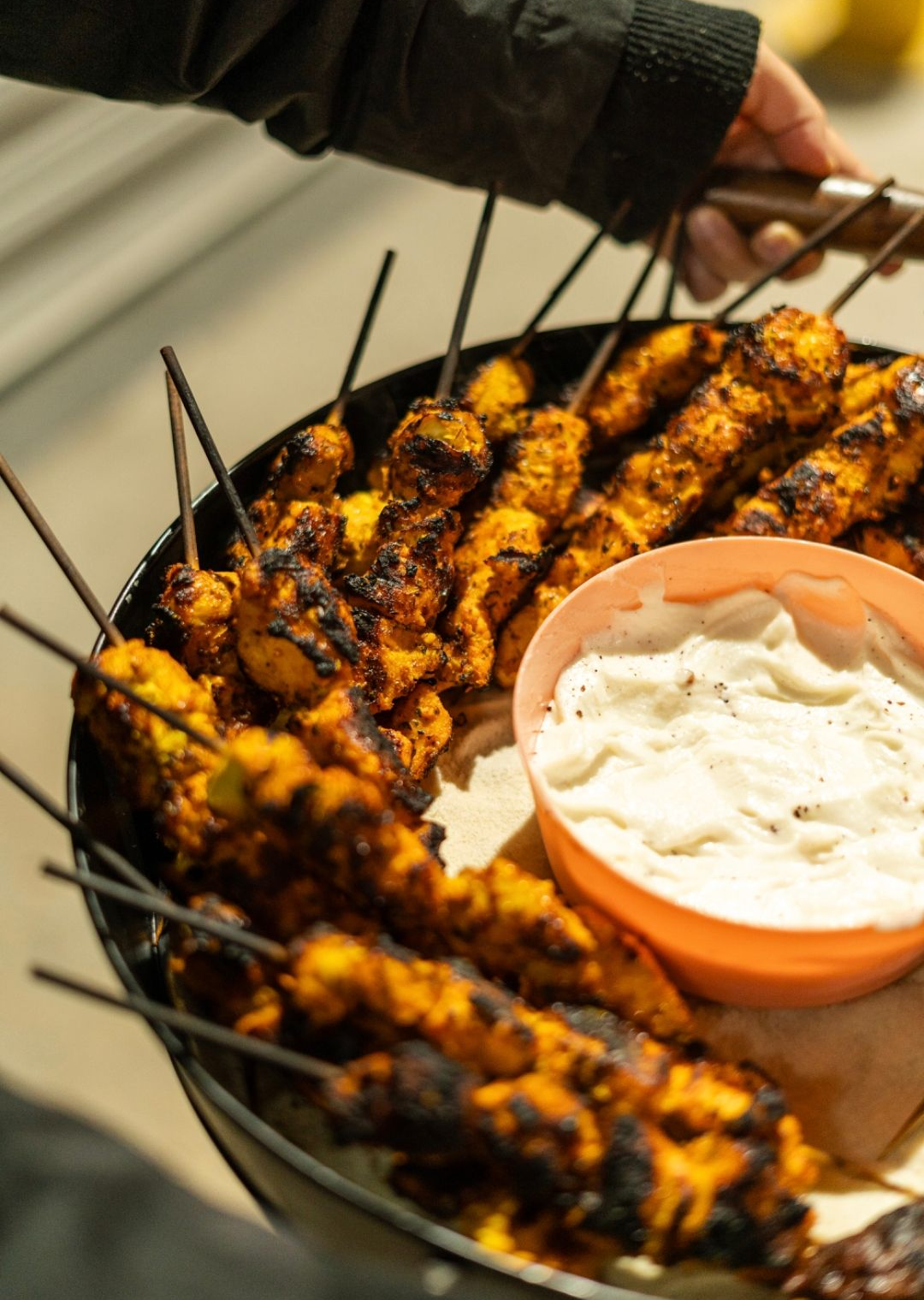 Grilled chicken skewers in a black tray, served with a side of white sauce. - The Habibiz Catering in Wingham NSW