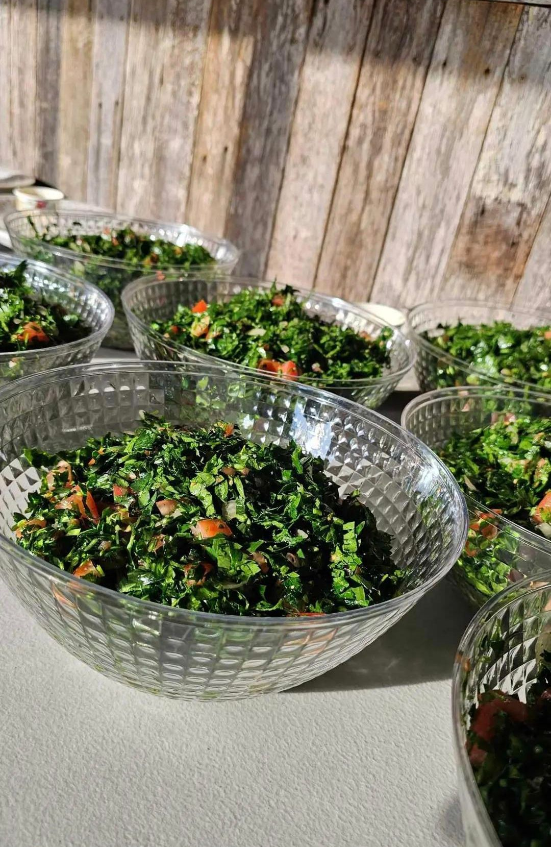 Bowls of tabbouleh salad on a table, with a wooden wall background. - The Habibiz Catering in Wingham NSW