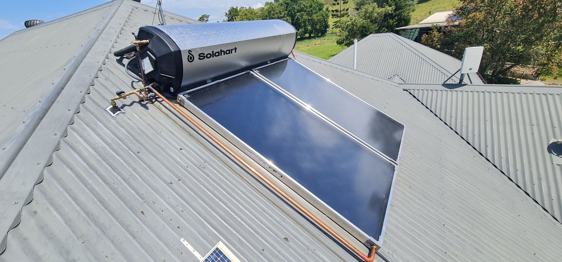 Solar water heater system on a rooftop, with panels and a silver tank against a blue sky.