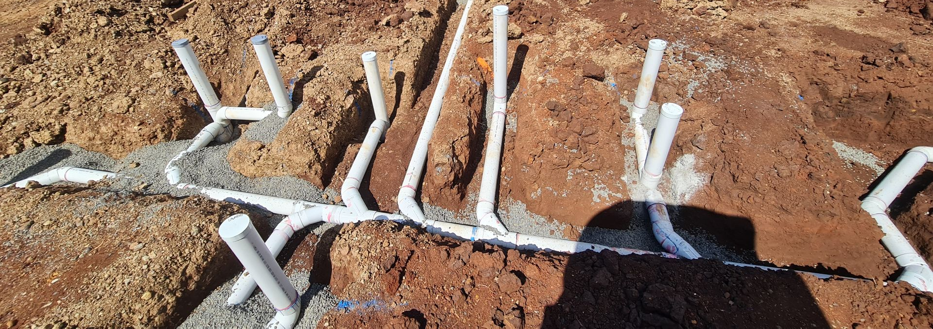 Construction site with buried white pipes and an excavator.